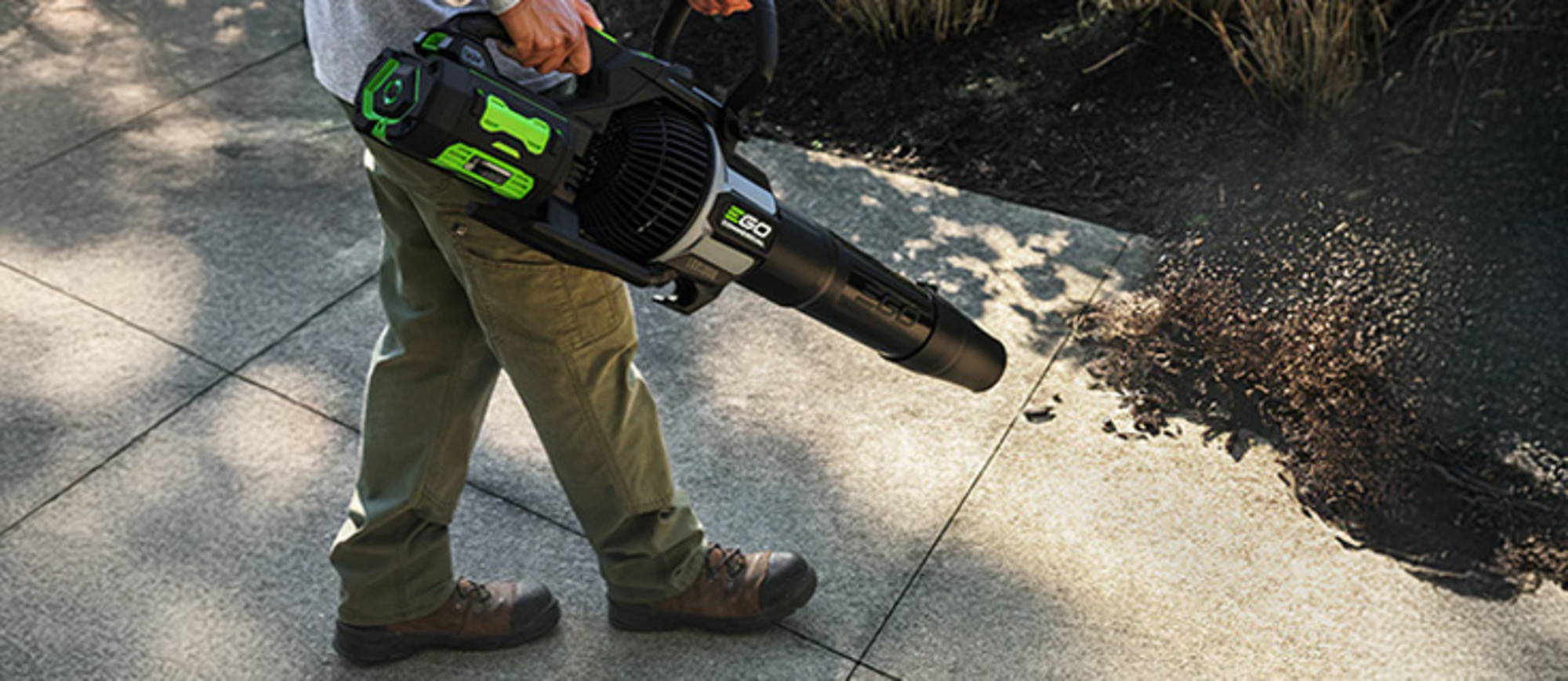 Ein Mann bläst mit einem EGO Laubbläser Laub von einer Terasse.