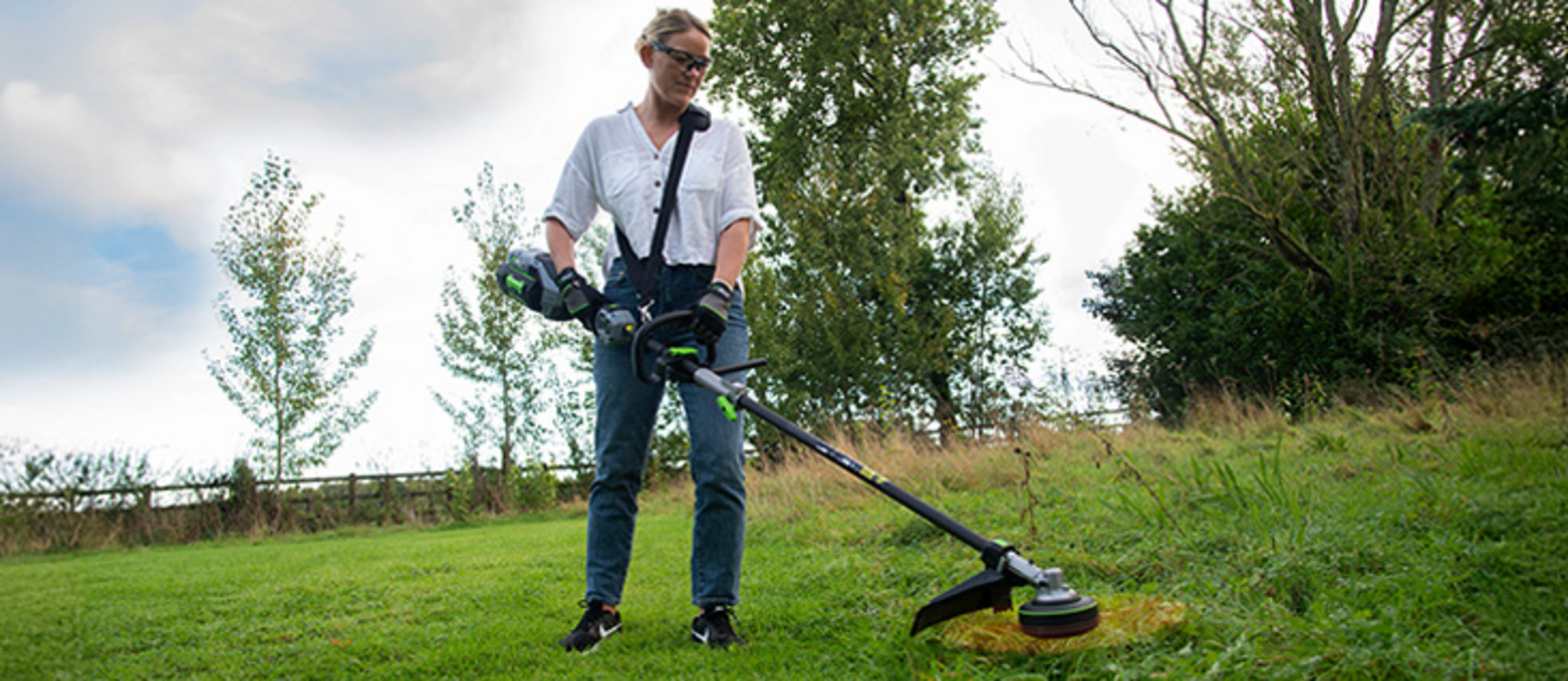 Eine Frau schneidet mit dem Multi-Tool-Aufsatz STA1700 von EGO Power+ Gras.