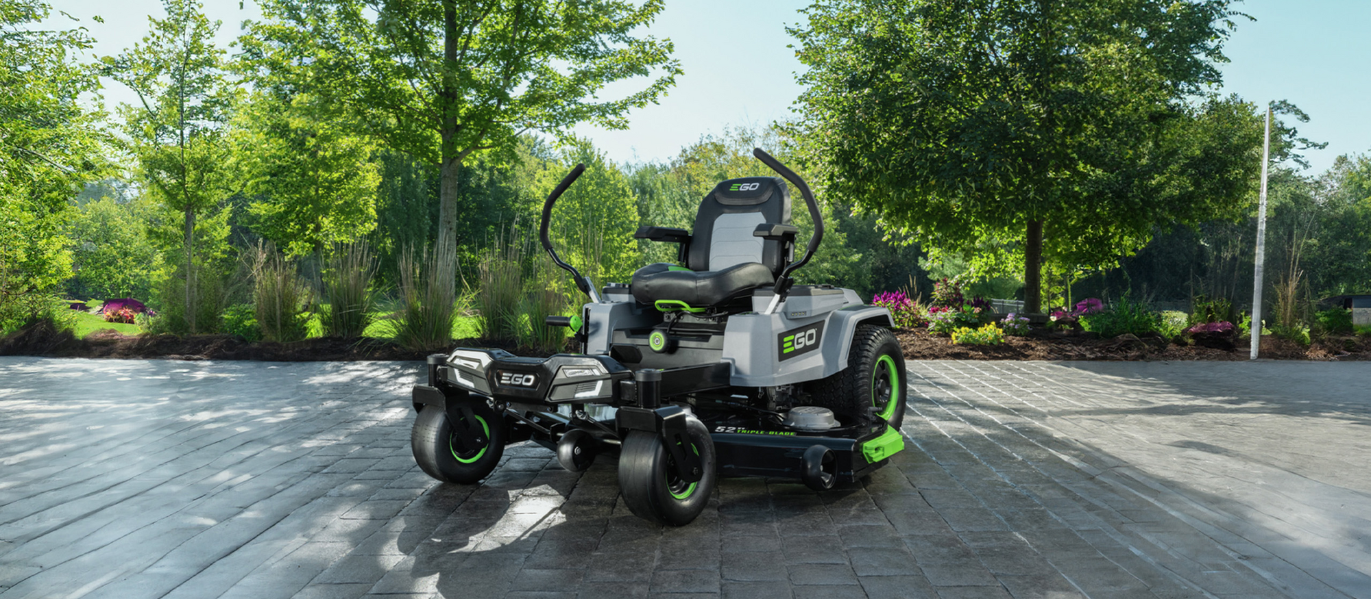 EGO Power+ Zero-Turn Aufsitzmäher steht auf einer gepflasterten Fläche mit Natur im Hintergrund.