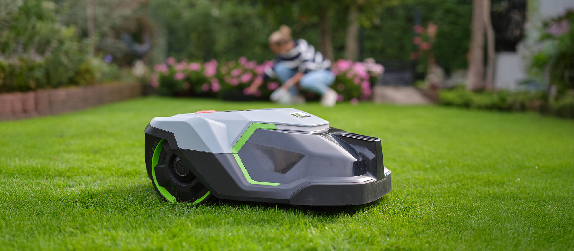 Der EGO Power+ Rasenroboter steht in einem Garten auf einer Wiese.