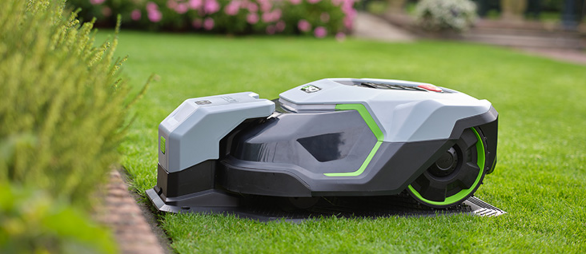 Rasenroboter von EGO Power+ in der Ladestation auf einer Rasenfläche.